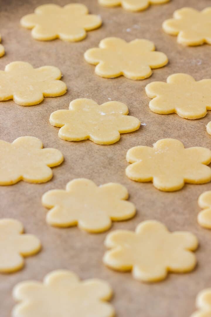Unbaked flower cookie shapes arranged on a parchment lined baking sheet.