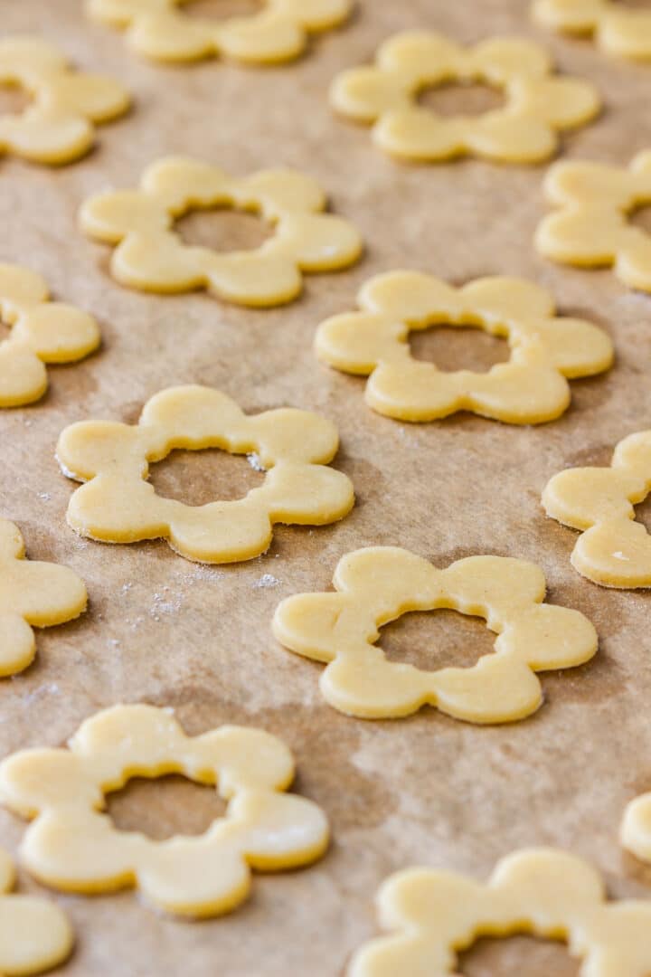 Flower cookie tops with center holes cut out, lined up on a baking sheet before baking.