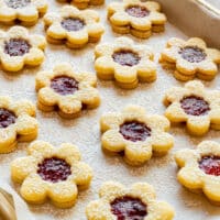 Tray of small flower Linzer cookies with strawberry jam centers, generously dusted with powdered sugar.