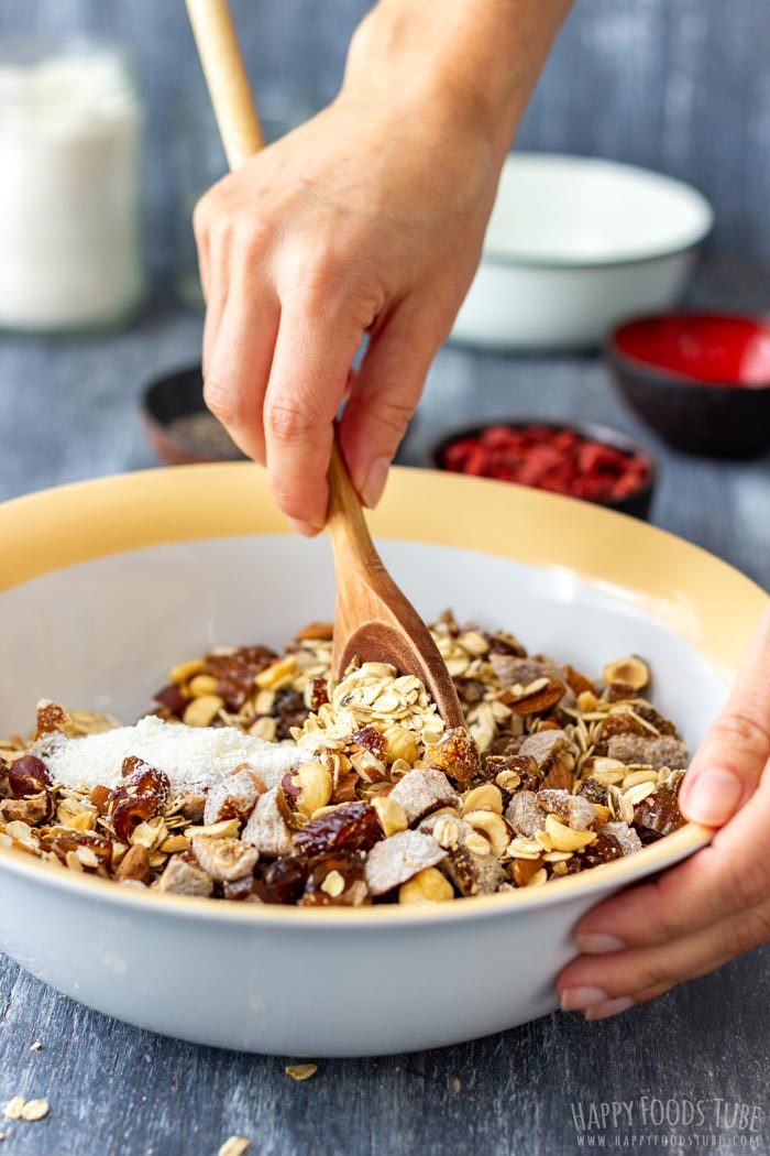 Mixing oats, nuts and dried fruit with shredded coconut using a wooden spoon.