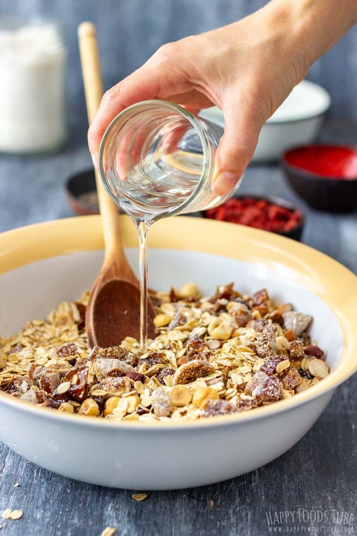 Pouring coconut oil into oat and nut mixture while preparing granola.