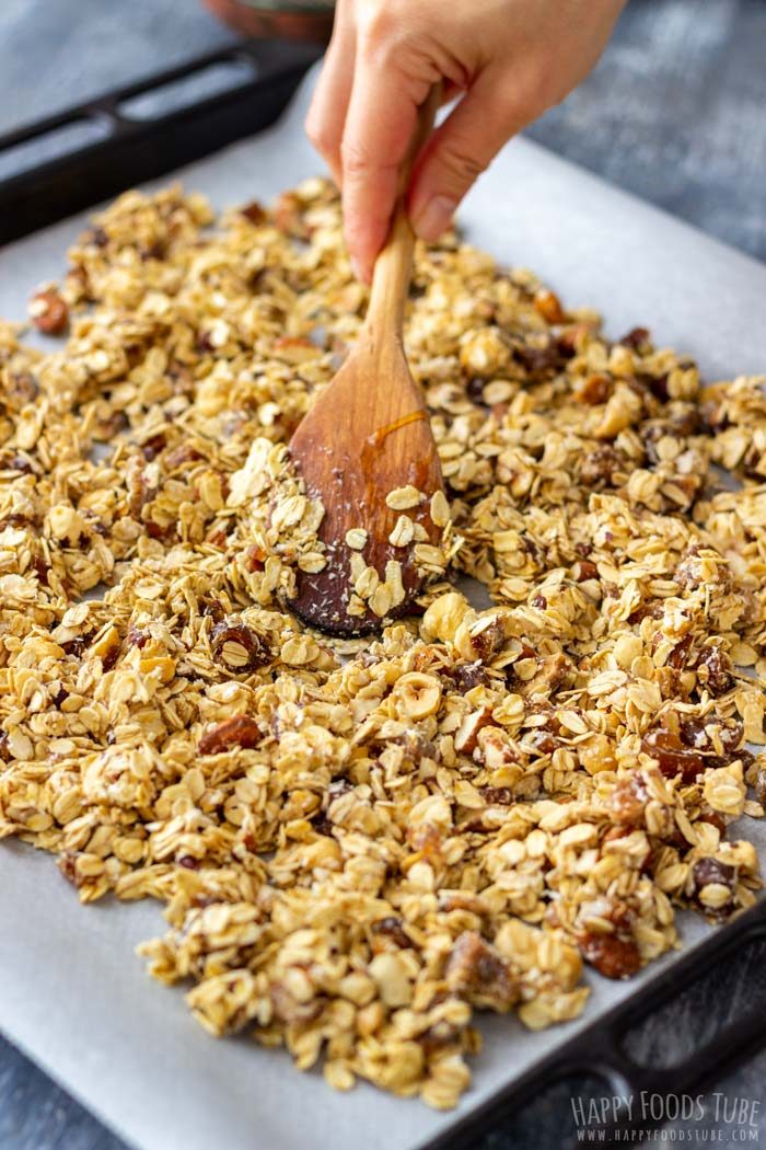 Spreading unbaked granola mixture onto a parchment-lined tray.