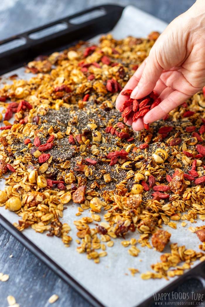 Adding goji berries and chia seeds to baked granola on a tray.
