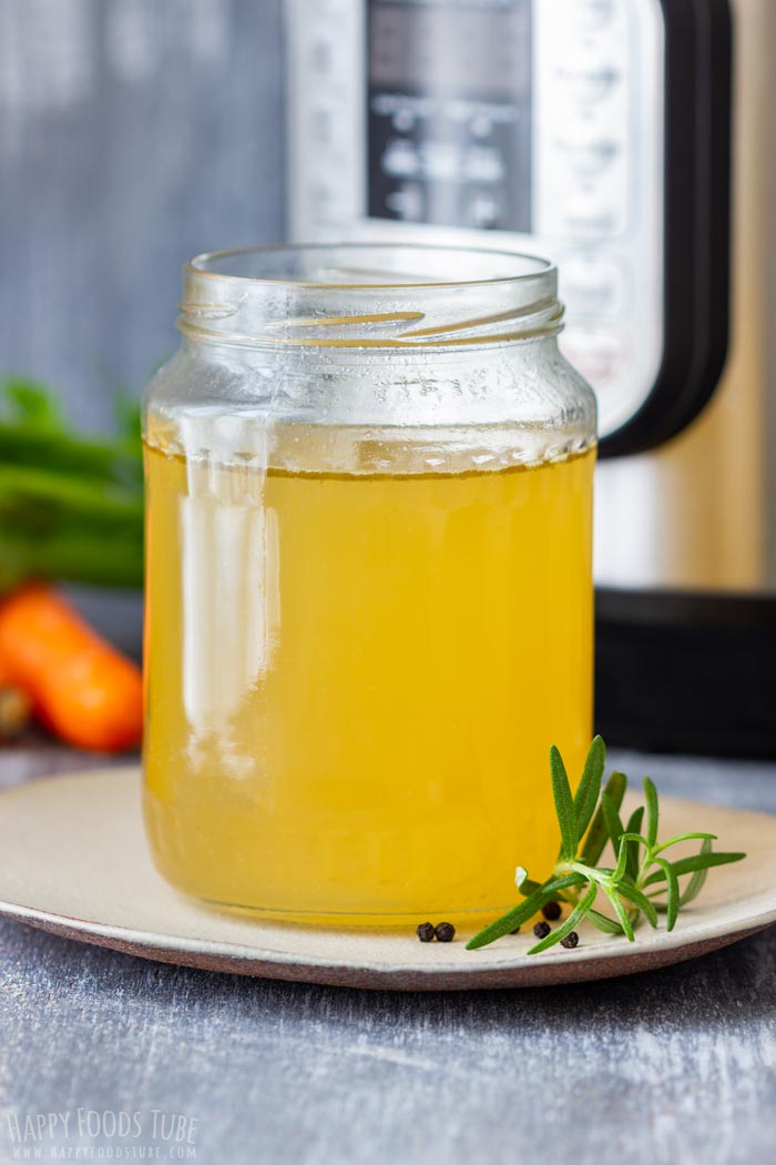 A jar of homemade turkey stock on a plate with herbs and peppercorns, with an instant pot in the background.