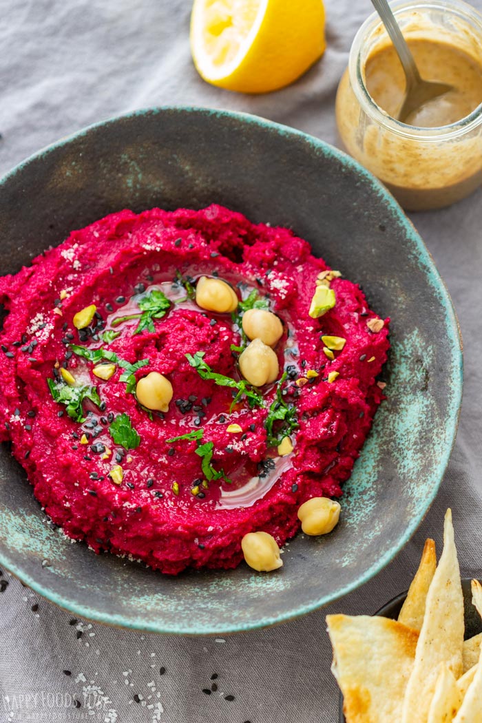 Rustic bowl of beet hummus garnished with chickpeas, herbs and seeds.