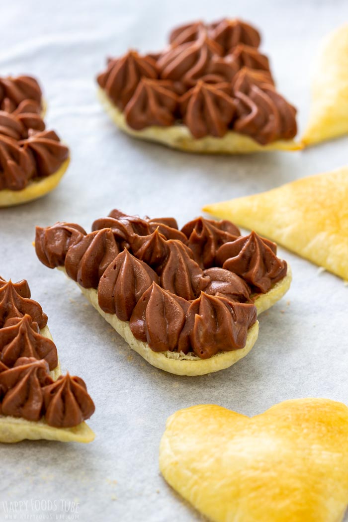Heart-shaped puff pastry topped with chocolate filling on parchment paper.