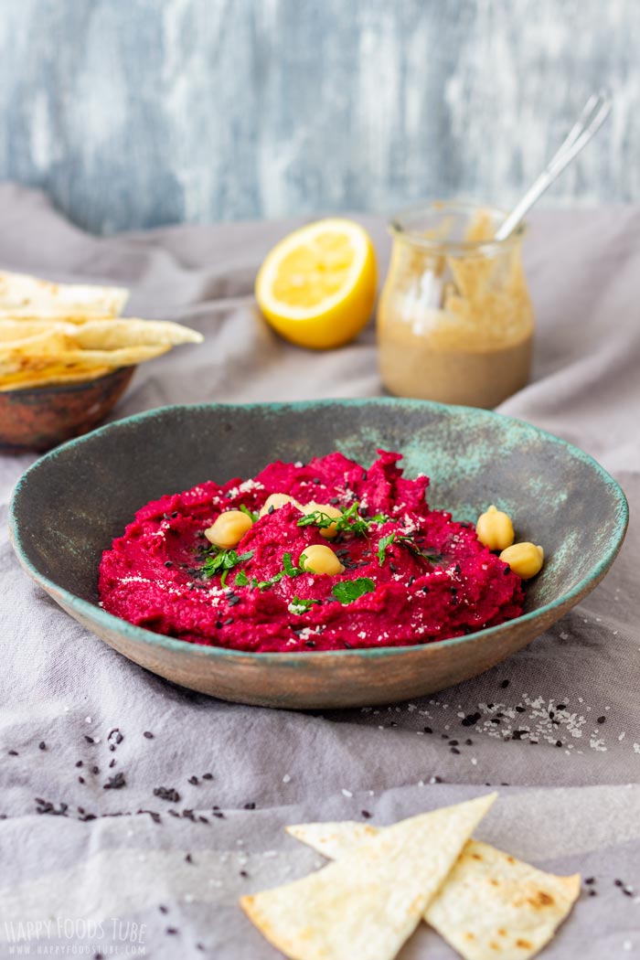 A bowl of vibrant beet hummus garnished with chickpeas and herbs, with tortilla chips.