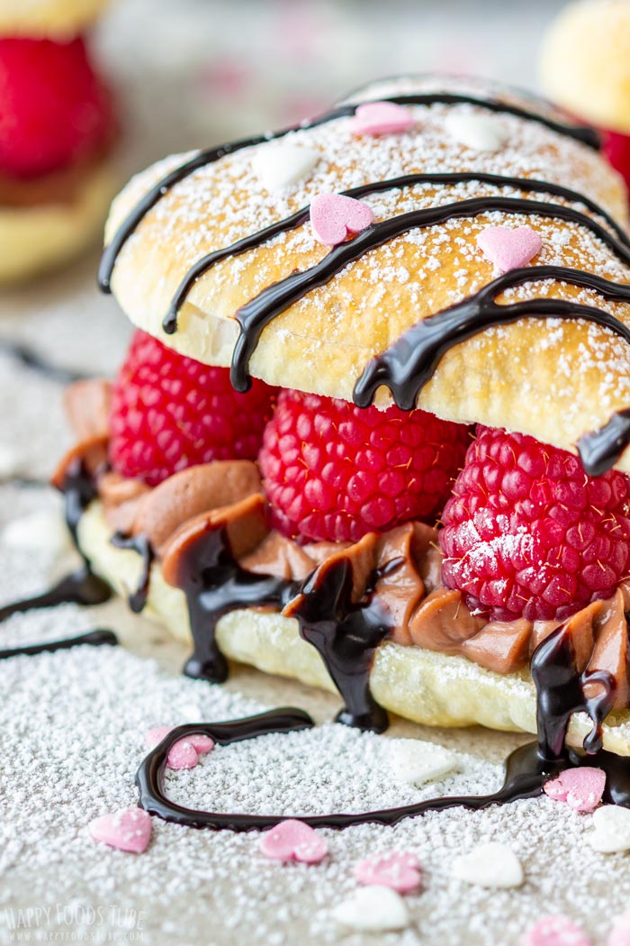 Elegant Valentine's Day pastry filled with raspberries and chocolate cream, topped with powdered sugar, chocolate drizzle and heart-shaped sprinkles.