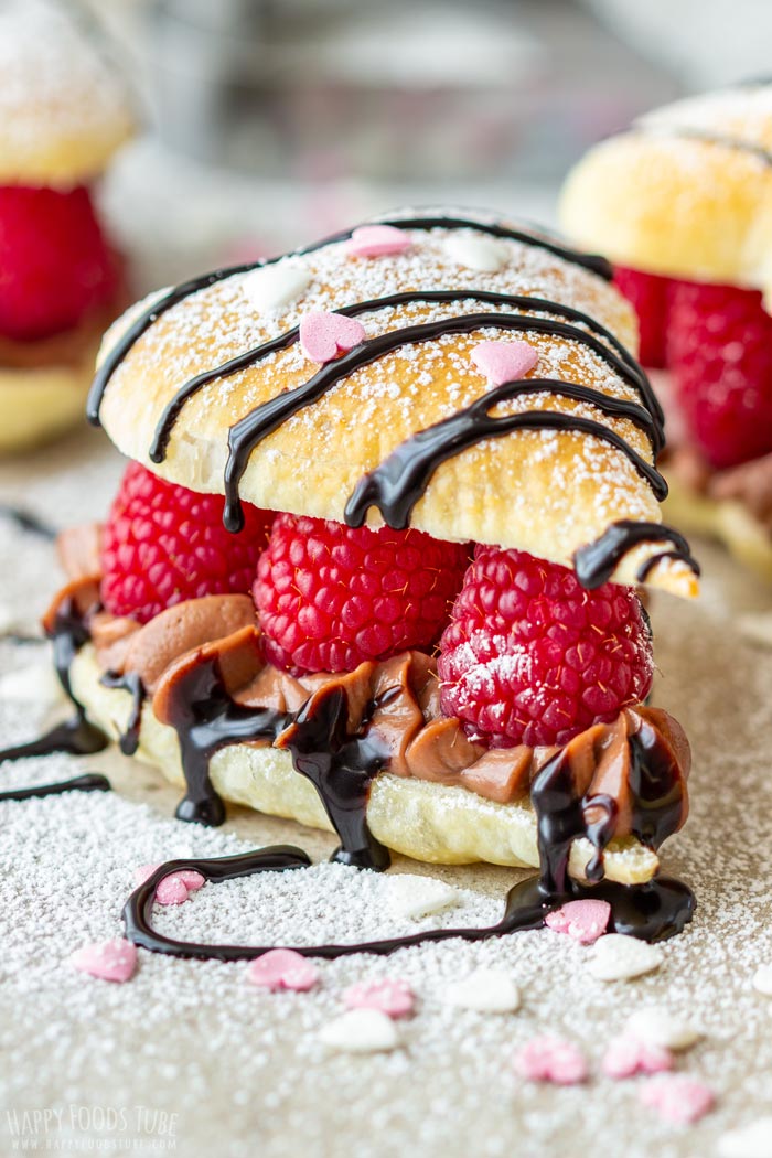 Valentine's Day puff pastry heart filled with raspberries, chocolate cream and drizzled with chocolate sauce, topped with powdered sugar and heart-shaped sprinkles.