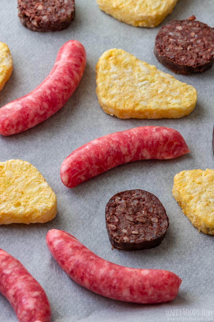 Raw sausages, black pudding and hash browns on a baking sheet, ready to cook.