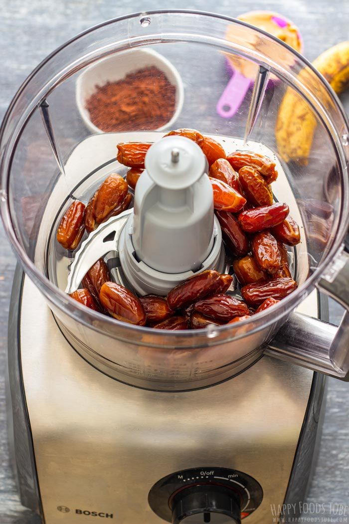 Pitted dates in the food processor with cocoa powder and a ripe banana in the background.