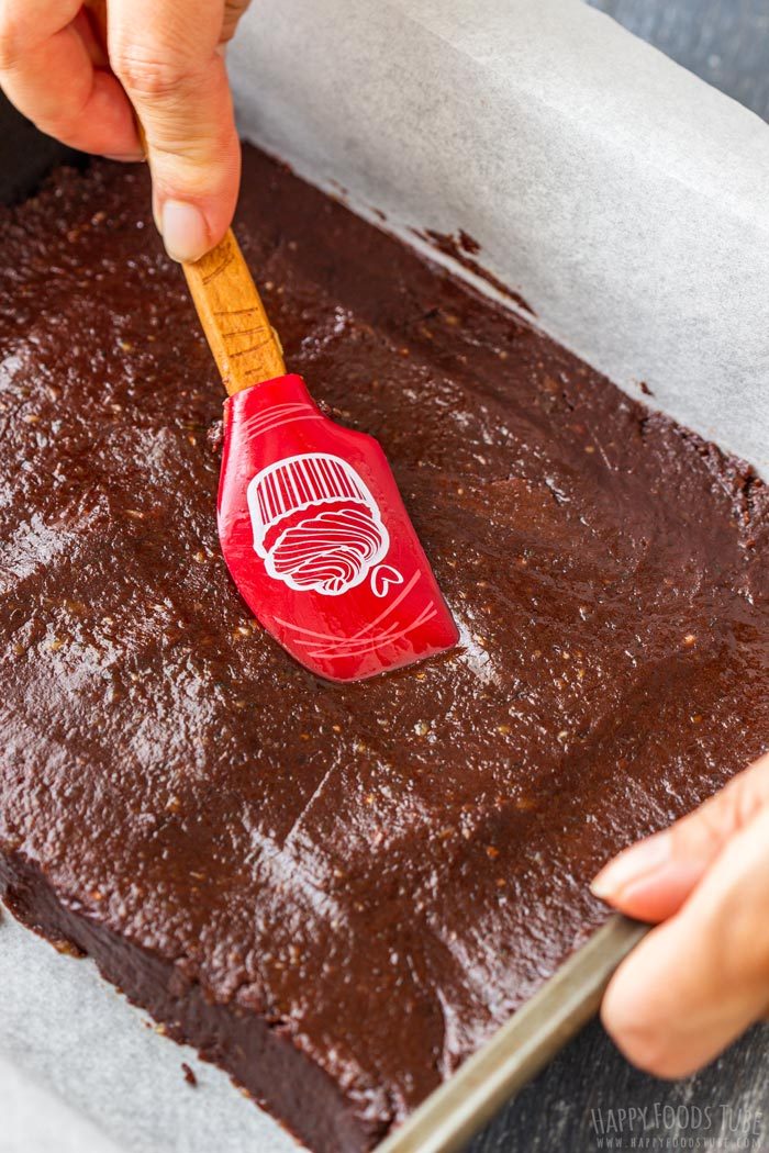 Brownie mixture being smoothed into a parchment-lined pan with a spatula.