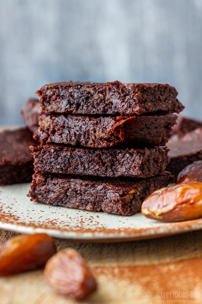 Four brownies stacked on a plate with dates beside them.