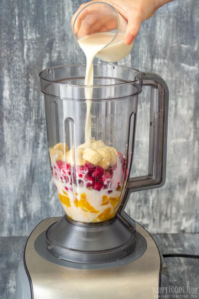 Almond milk being poured into a blender with oranges, banana and frozen cranberries.