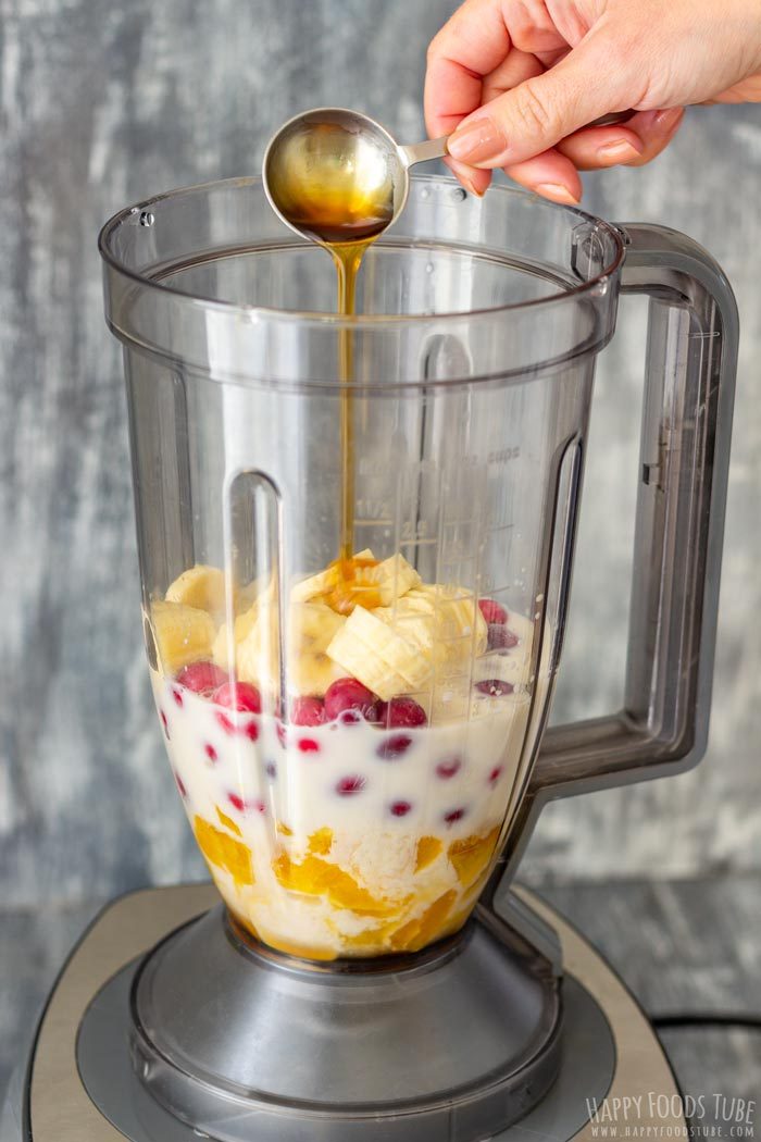 Maple syrup being poured over the fruit and almond milk in a blender.