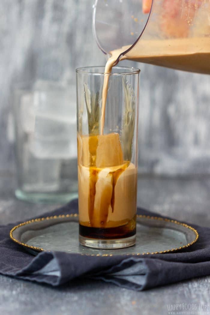 Pouring the latte over large ice cubes into a caramel-lined glass.
