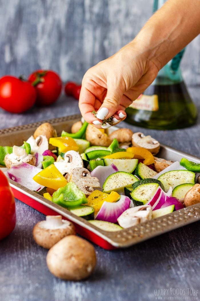 Dried oregano sprinkled over chopped vegetables seasoned with salt and pepper in a tray.