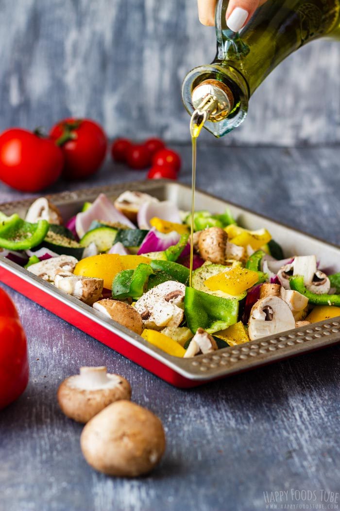 Olive oil poured over chopped peppers, zucchini, mushrooms and onion in a baking tray.