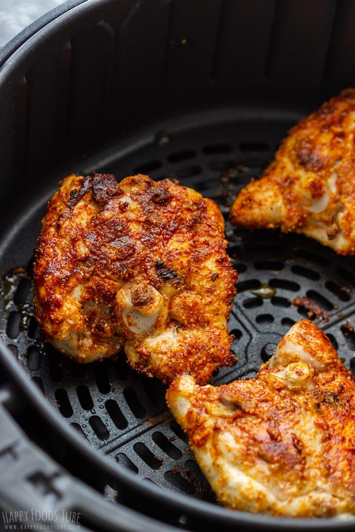 Seasoned chicken thighs browning in an air fryer basket with a crisp, golden spice crust.