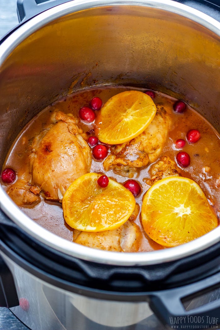 Chicken thighs cooked in a sauce, garnished with slices of orange and whole cranberries.
