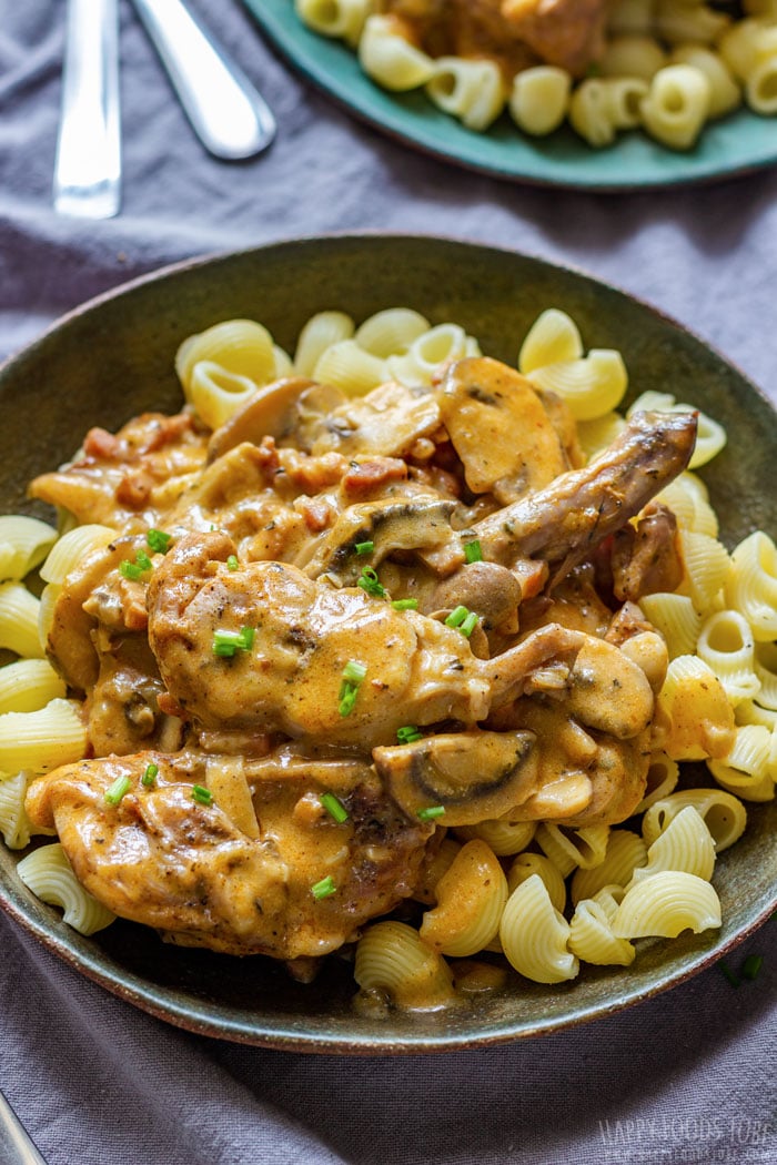 A bowl of pasta topped with creamy rabbit and mushroom sauce, garnished with chopped chives.