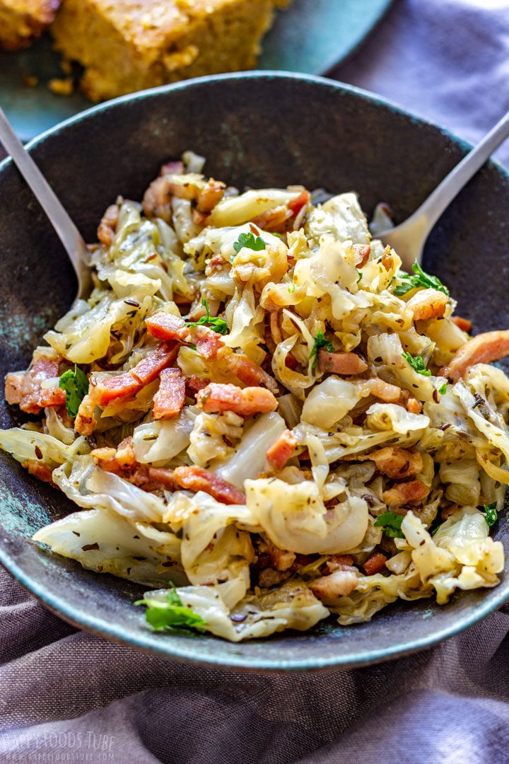 Bowl of cabbage and bacon with two serving spoons.