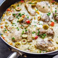 Close-up of creamy boneless skinless chicken thighs with olives and peppers in a creamy skillet sauce.