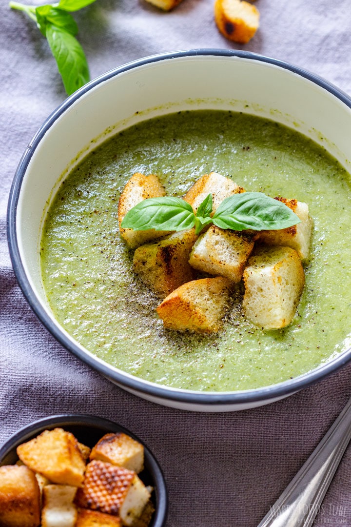 A bowl of green soup garnished with croutons and fresh basil leaves.