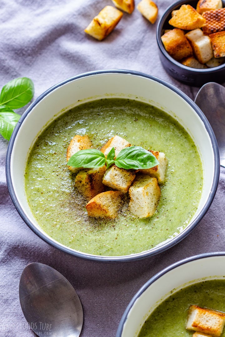A bowl of homemade broccoli and celery soup with croutons and basil leaves.