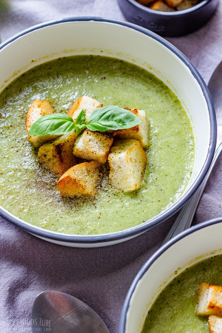 A bowl of broccoli celery soup garnished with croutons and basil leaves.