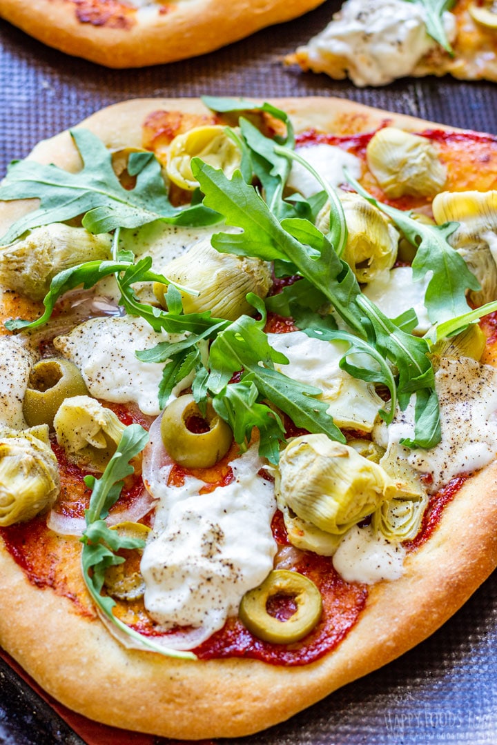 Burrata cheese pizza topped with artichoke hearts, olives and arugula