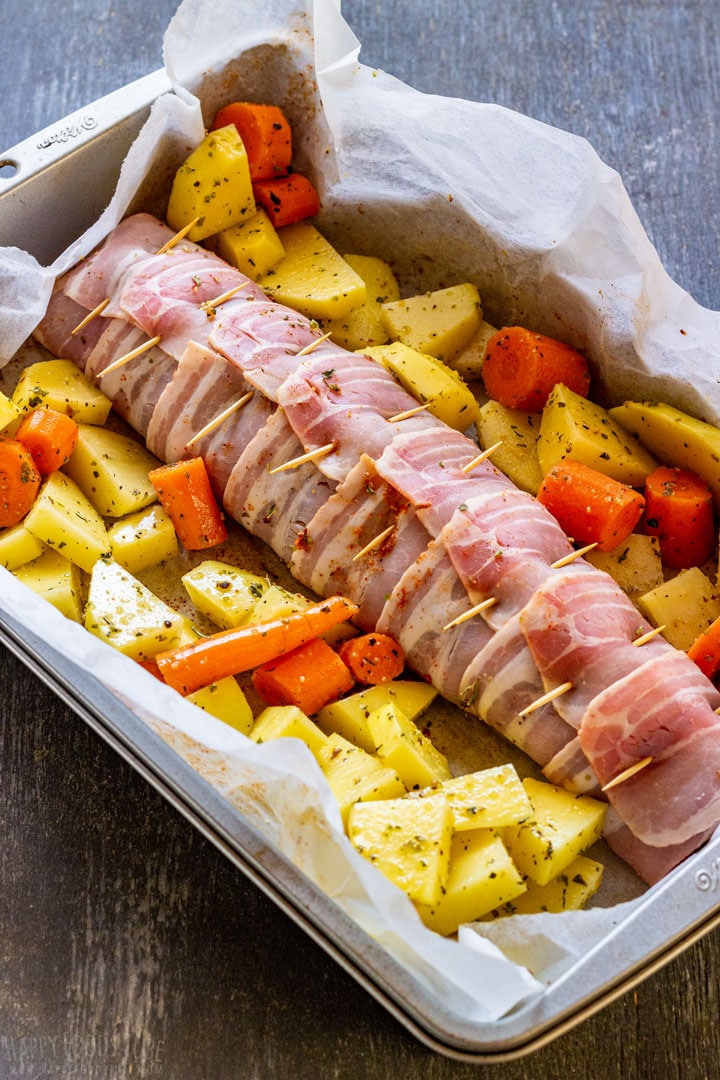 Pork tenderloin wrapped in bacon with veggies and ready to be cooked