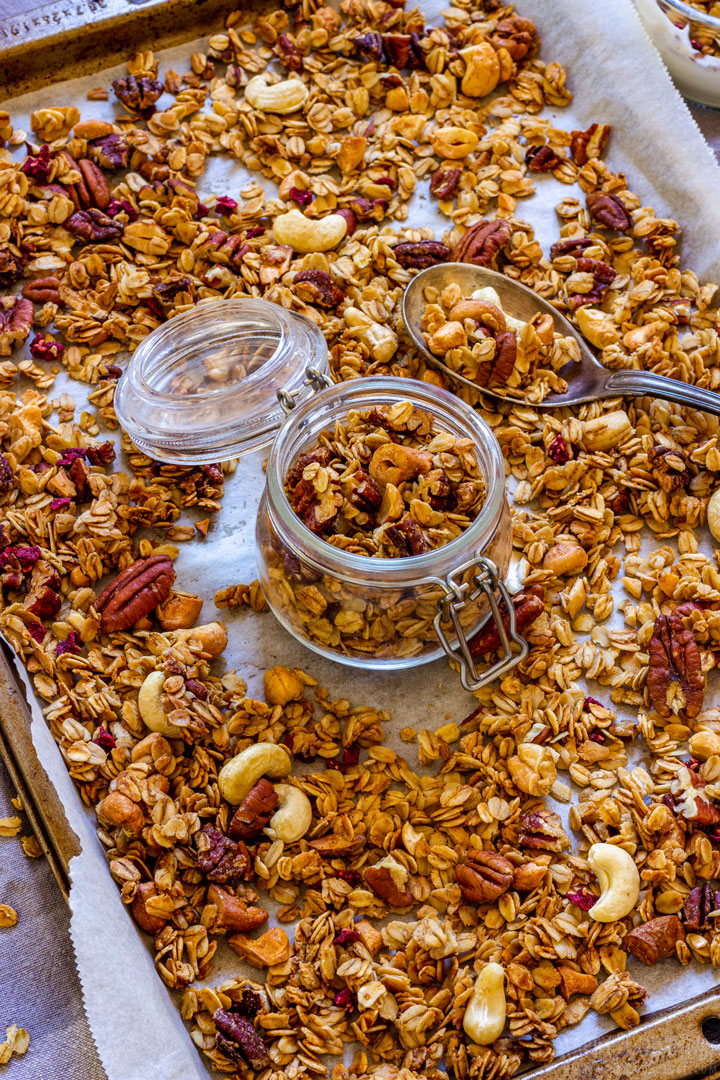 Freshly made granol on the baking tray with a jar and spoon