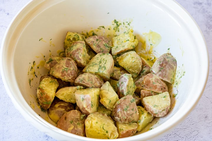 Potatoes mixed with potato dressing and dill in a large bowl