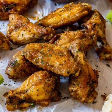 Pile of crispy garlic parmesan chicken wings on parchment, sprinkled with parsley.