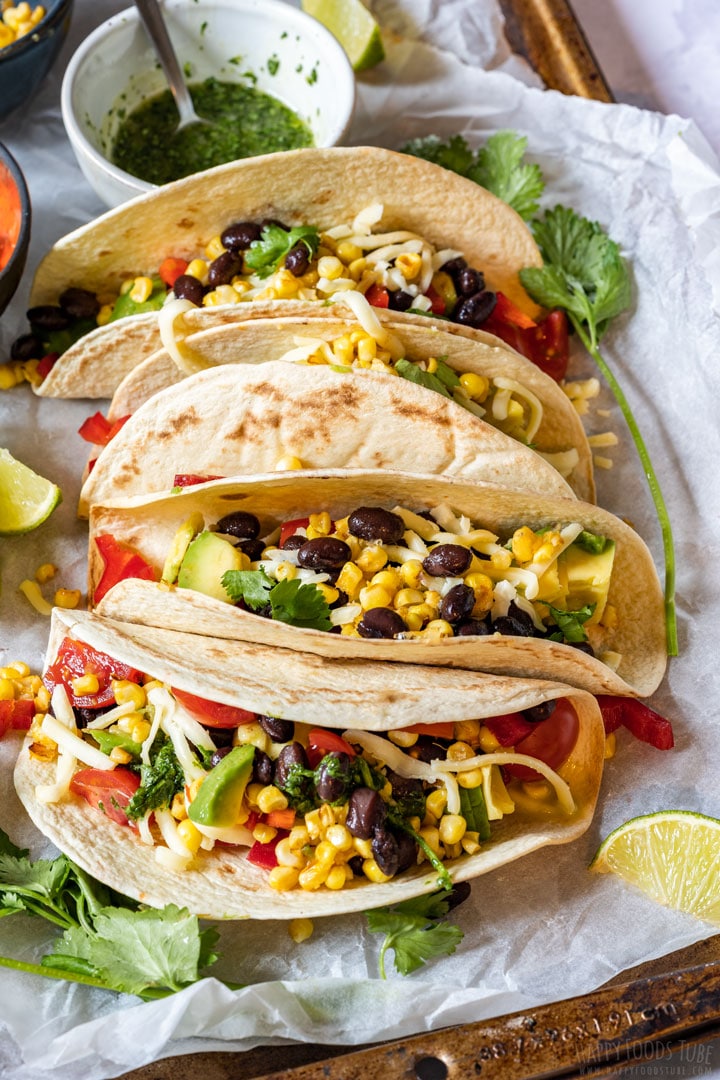 Vegetarian tacos with black beans, avocados, tomatoes and cheese with lime wedges