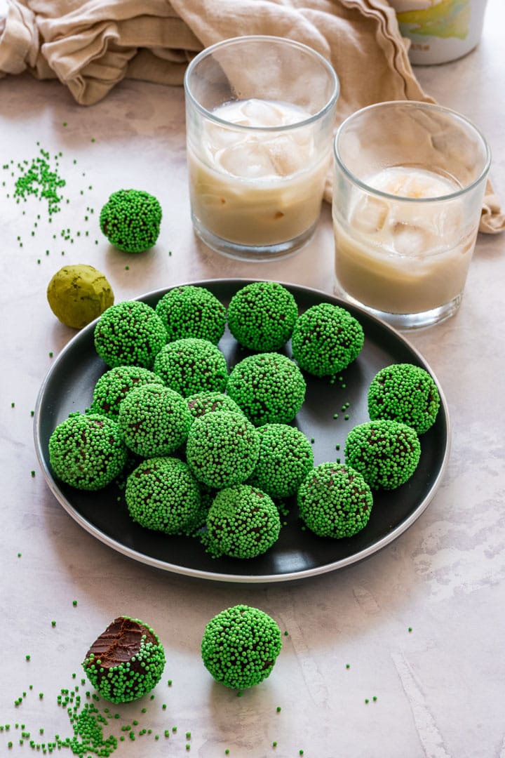 Plate of Irish cream chocolate truffles coated in green sprinkles with two glasses of creamy Irish Baileys.