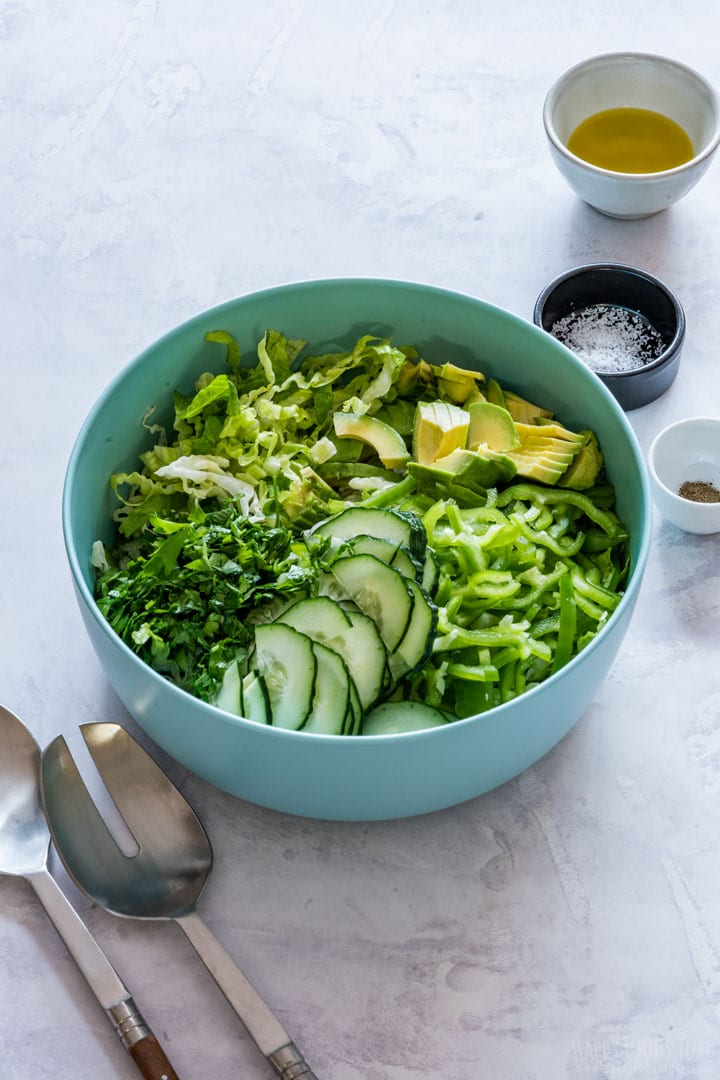 Sliced lettuce, cucumber, avocados and parsley in the bowl.