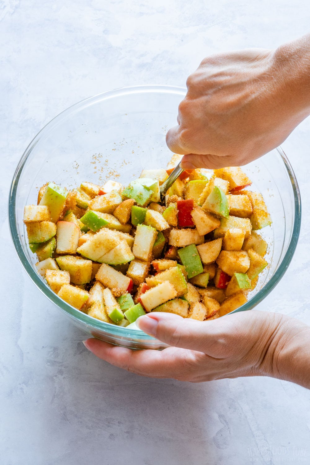 Mixing diced apples with brown sugar in the glass bowl.