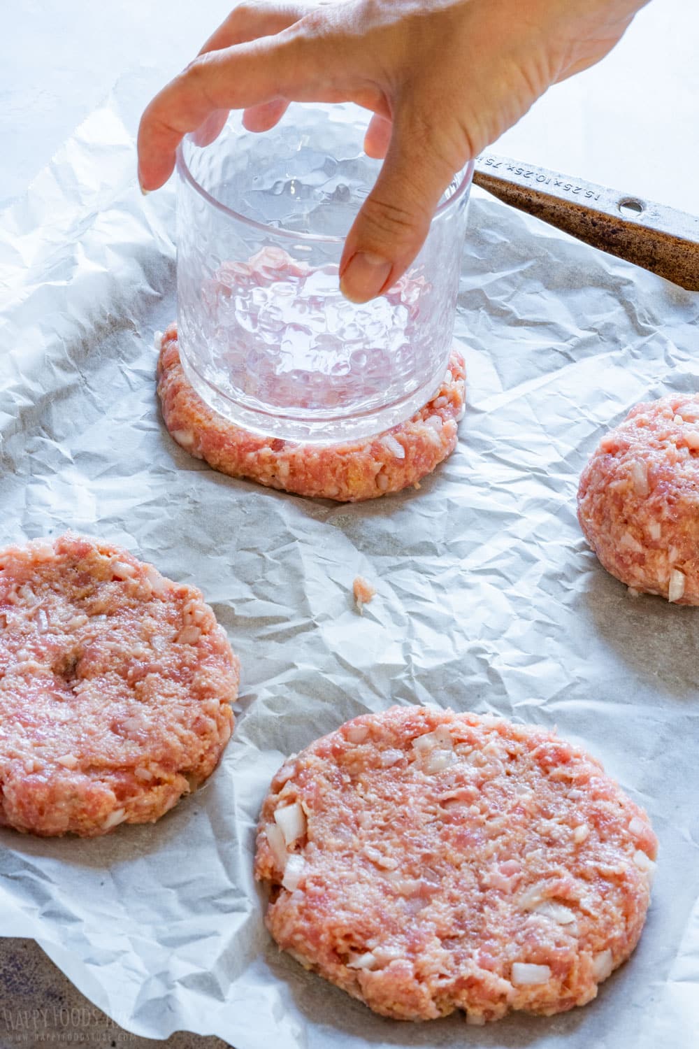 Flattening burger patties with large glass.