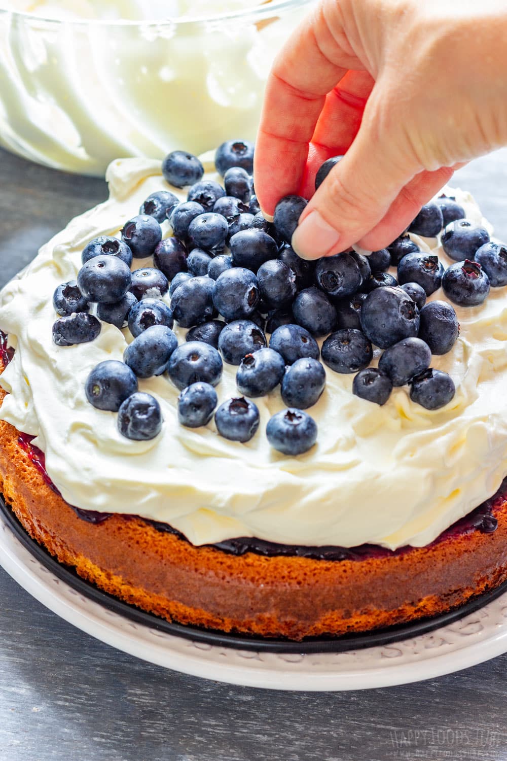 Adding fresh blueberries by hand to layered cream cake.