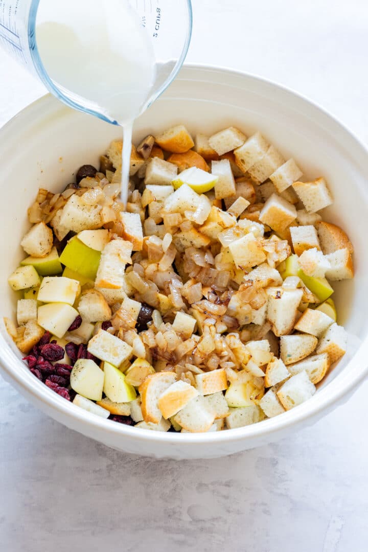 Stock being poured over sautéed onions, apples and bread in a mixing bowl.