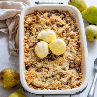 Large baking dish with golden brown pear crisp topped with yellow vanilla ice cream.