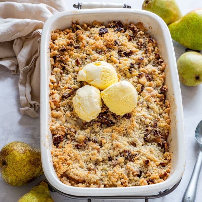 Large baking dish with golden brown pear crisp topped with yellow vanilla ice cream.