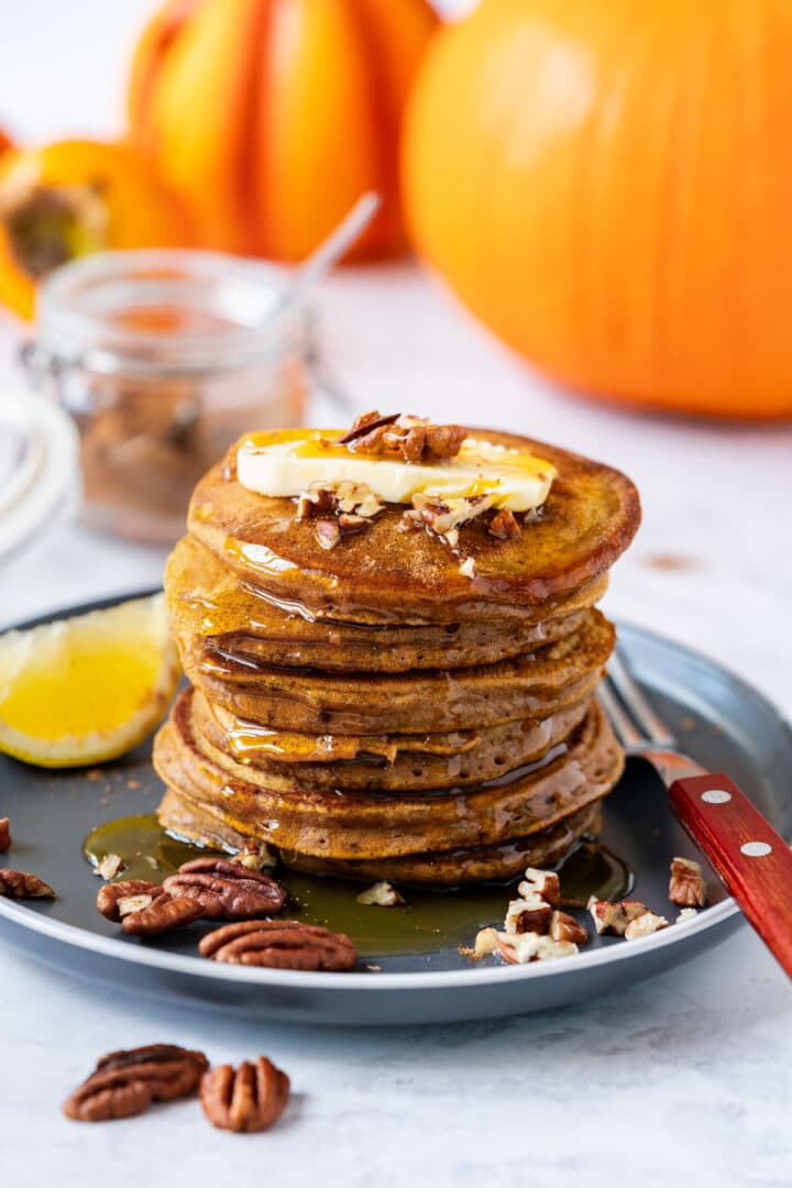 Delicious pumpkin pancakes on a plate, jar of pumpkin pie spice in the background.