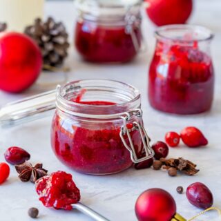Jars of homemade Christmas jam with spices and cranberries on a light surface.
