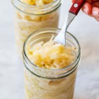 Close-up of homemade sauerkraut in a glass jar with a fork lifting a portion, showing fermented cabbage.