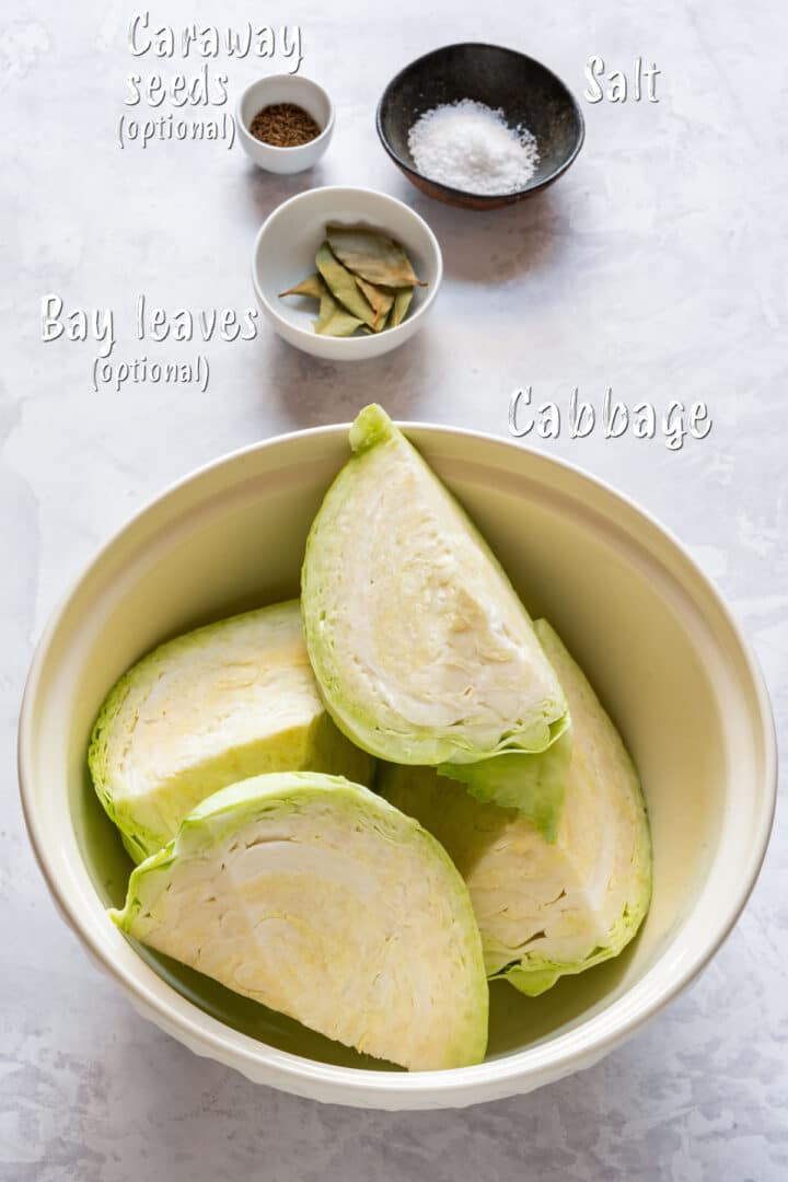 Ingredients for homemade sauerkraut: cabbage, salt, bay leaves and caraway seeds on a marble countertop.