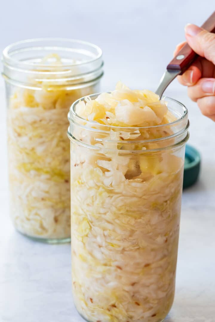 Julia scooping homemade sauerkraut from a glass jar with a fork, showing its fermented texture.