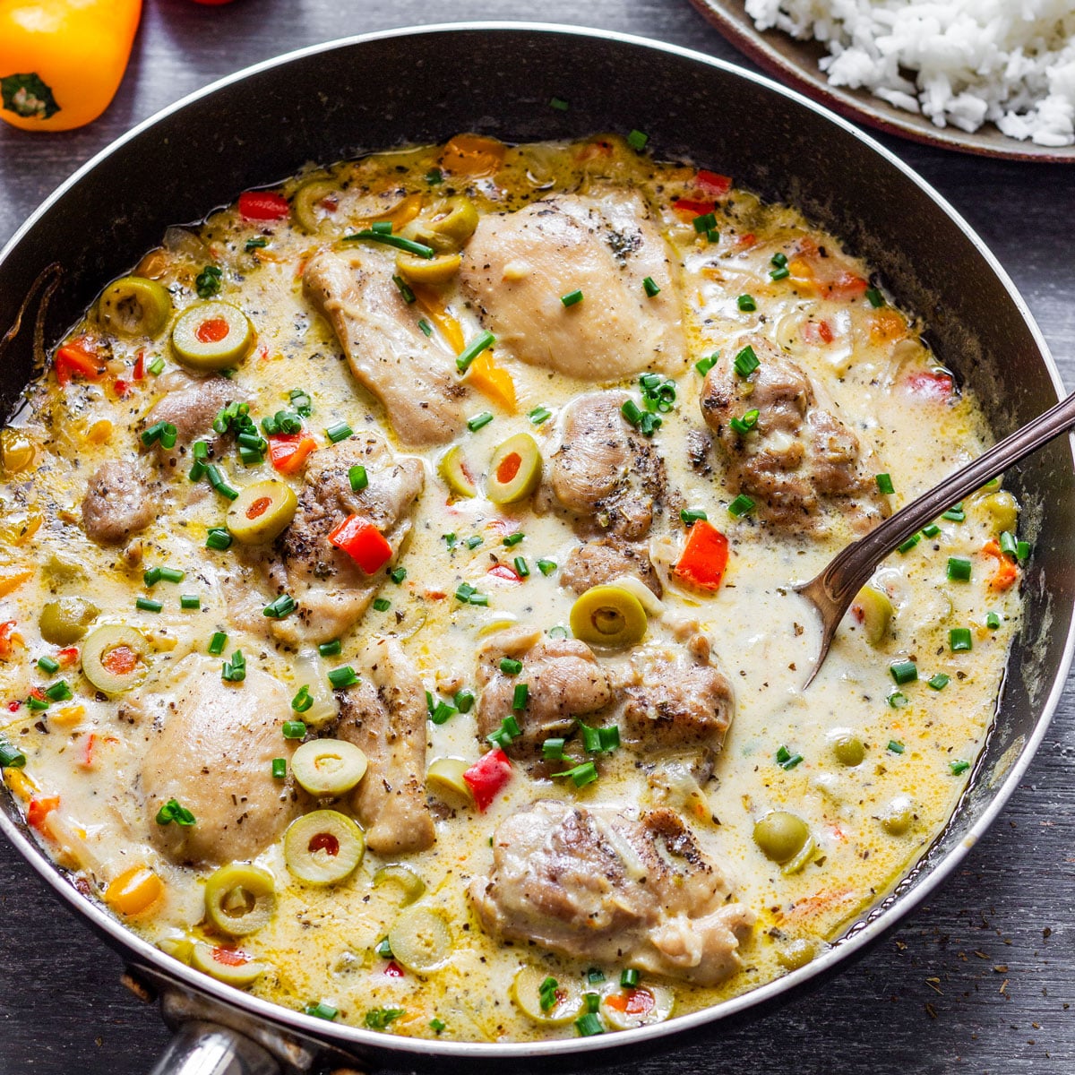 Skillet of creamy chicken thighs with olives and peppers.